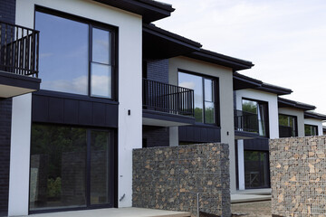 Many modern white cottages with panoramic windows on the background of the park and blue sky.