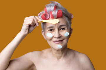 cute elderly grandmother in curlers applies cream face mask