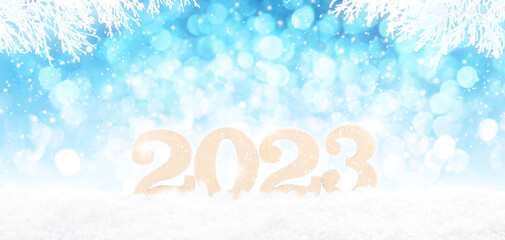 Wooden 2023 Numbers in perspective on bright blue bokeh winter background with white snowy branches and falling snow.