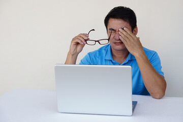 Asian man, feels hurt his eyes, holds eyeglasses during working on laptop. concept : Eyesight...