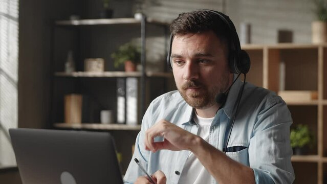 Concentrated young male worker employee entrepreneur in headphones, holding negotiations meeting online with client or colleagues, using computer video call app