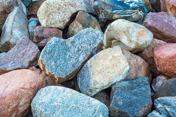 Close-up of a pile of large granite stones with a fine texture. Background with a protective embankment of pebbles on the beach.