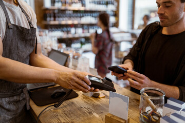 Midsection of male owner giving credit card machine to customer doing online payment at store