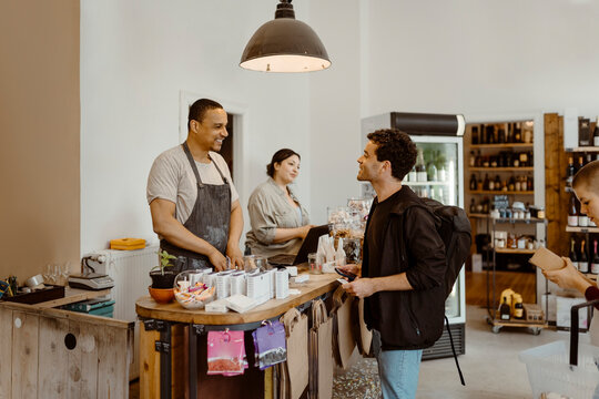 Side view of male customer interacting with store owner standing at checkout counter