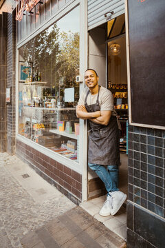 Smiling male owner with arms crossed leaning at shop doorway
