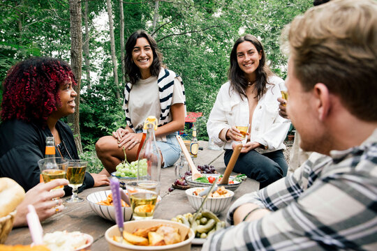 Smiling women talking to friends with food on table during garden party in back yard