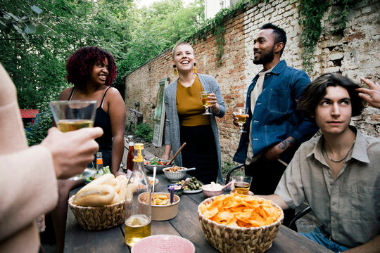 Multiracial male and female friends enjoying food and drinks at garden party