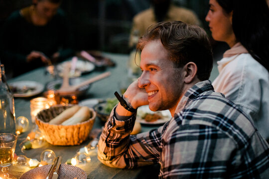 Side view of smiling young man leaning on elbow at dining table during sinner party