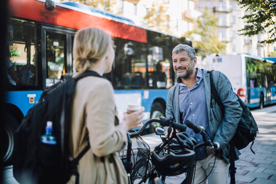Male and female business colleagues with bicycles talking to each other at street