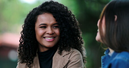 African girl listening to friend in conversation outside, diverse female friends talk at park