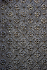 An old metal door, forged gates, rivets on the facade of a cast-iron door, a round handle to open the door, the texture of old iron.