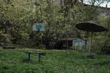 Soviet playground in with rusted basketball hoop, shed, and wooden park bench