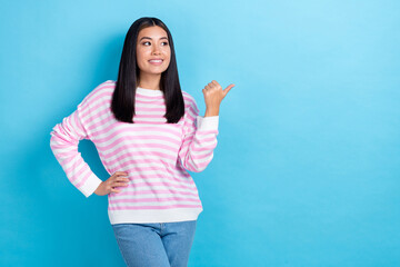 Photo of cute dreamy lady wear striped sweater looking pointing thumb empty space isolated blue color background