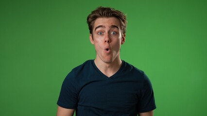 Portrait of amazed young man 20s shocked, saying WOW then give thumbs up. Handsome guy surprised isolated on solid green screen background
