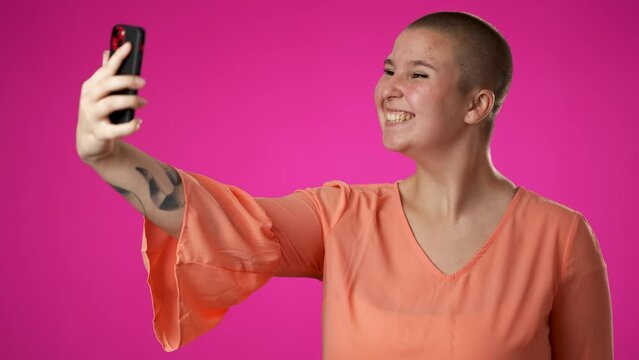 Copy space portrait of happy smiling gender fluid non binary young woman 20s using speaking talking on mobile cell phone conducting pleasant conversation isolated on pink background studio. 