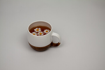 Obraz na płótnie Canvas Chamomile tea in a white clay cup on a light background