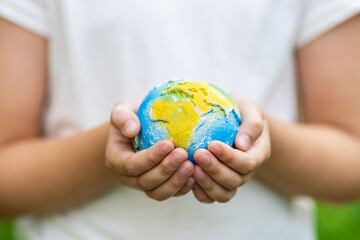 Kid holding small planet in hands against spring or summer green background. Ecology, environment and Earth day concept. 