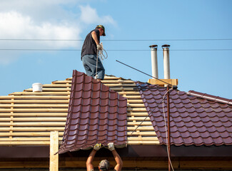 Workers install metal roofing on the wooden roof of a house.