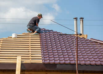 Workers install metal roofing on the wooden roof of a house.