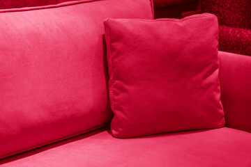 Close-up of cushion on cozy sofa. Pillow on casual couch in living room. Image toned in trendy color of year 2023 Viva Magenta.