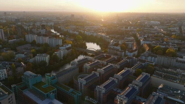 Forwards fly above urban borough with river and autumn colour foliage on trees. Aerial view against setting sun. Berlin, Germany