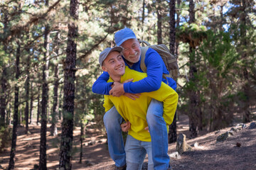 Handsome boy carries his grandfather on shoulders as he walks happily in the forest. Smiling...