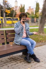 Young indian man sitting in the bench with coffee using mobile phone