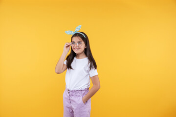 Studio portrait smiling 10, 11 years old kid girl. Teenager child wearing glasses posing on yellow...
