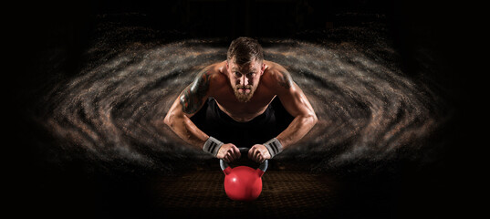 Muscular man doing push ups on red kettlebell