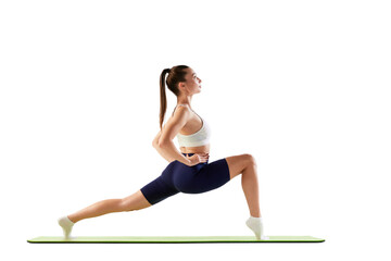 Portrait of young sportive woman training, doing legs stretching exercises on mat isolated over white background. Concept of sport, fitness, health