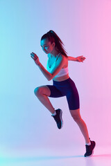 Fototapeta na wymiar Portrait of young sportive woman training, doing running exercises isolated over gradient blue pink background in neon light. Concept of sport, fitness, health