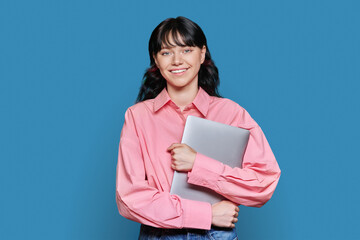 Obraz premium Teenage female student with laptop, looking at camera on blue background