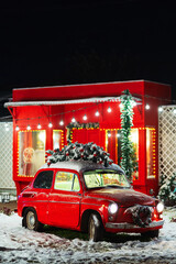 a red car with a Christmas tree on the roof against the backdrop of a red shop. old red car with...