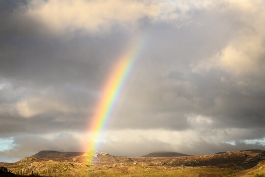 A dramatic, cloudy, sunlit, autumnal HDR image of a rainbow over Sutherland in north west Scotland.