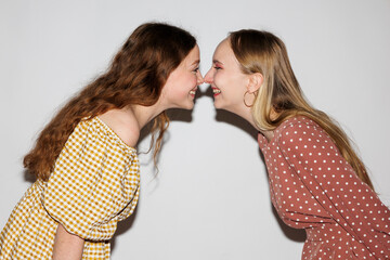 Two young cheerful women touch each other with their noses on a white background.