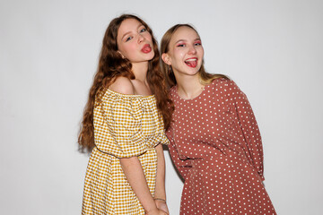 Two young women cheerfully show their tongues on a white background.