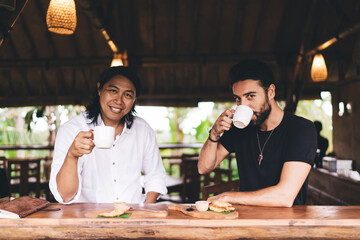 Cheerful diverse travelers sitting and drinking coffee in cafe