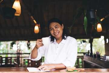Cheerful ethnic man sitting at table with cup of coffee in cafe