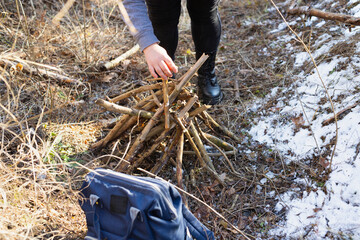 Obraz premium Woman traveler in nature journey on sunny day trying to make bonfire using dry stick she found in the forest, woman travels alone.