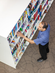 College Library: Reference Books. A mature South Asian man browsing the shelves of an academic...