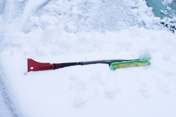 Winter. A snow brush lies on the hood of a car covered with snow.