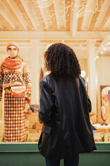 Shot of girl from the behind. She is looking in the store window to buy a new dress.