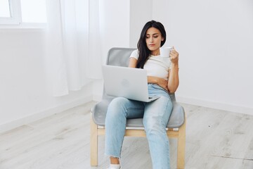 Woman relaxing at home sitting on a chair and watching a movie on her laptop with a cup of tea, smile autumnal mood