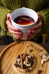 The girl is holding a cup of hot mulled wine. Close-up on the background of spices for making a drink
