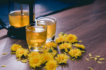 Chrysanthemum tea in glass on wooden table and flowers with sun light and black background,Healthy...