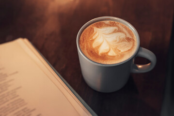 A cup of coffee with an open book on a wooden table. Drink coffee and read a book in a cozy warm...