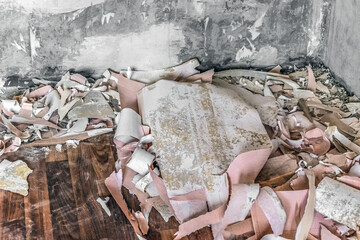 Pile of torn paper pink wallpaper on a brown wooden floor and old worn walls in the room. Paper...
