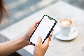 A mockup of a woman's hand holding a mobile phone in a cafe
