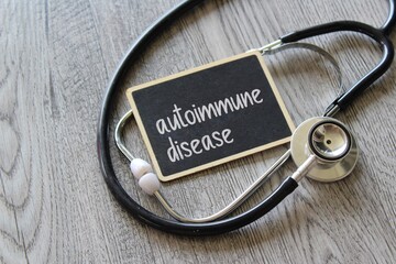 Stethoscope and chalkboard with text AUTOIMMUNE DISEASE on wooden table. Medical and healthcare...
