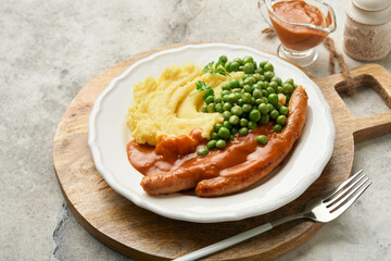 Bangers and mash. Grilled sausages with mash potato and green pea on white plate on grey background. Traditional dish of Great Britain and Ireland. BBQ beef sausages. Top view.
